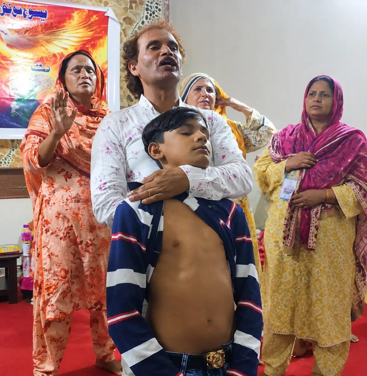 Pastor Yousaf Hussain praying with a family at Church of Christ Assembly in Pakistan
