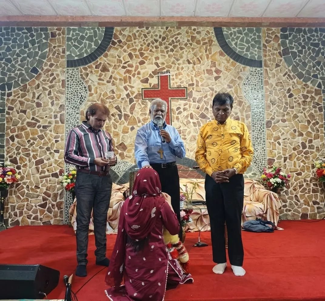 Pastor praying with church members before the cross at Church of Christ Assembly in Pakistan