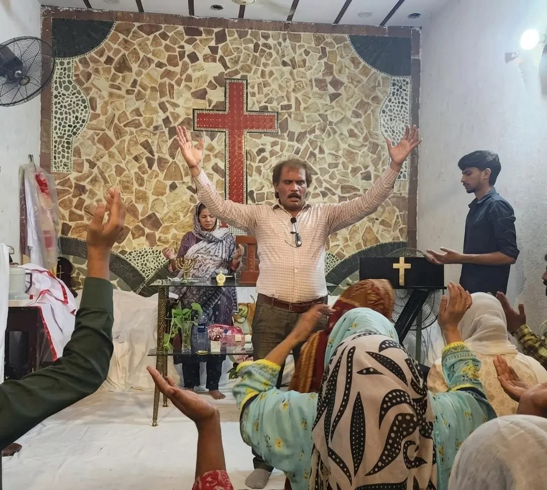 Pastor leading worship before the cross at Church of Christ Assembly in Pakistan